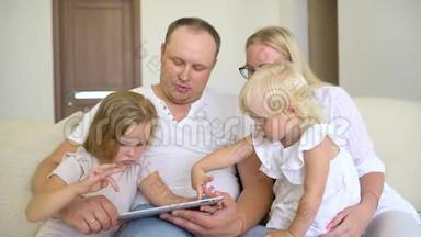 快乐的家庭<strong>一起玩</strong>笔记本电脑和数字<strong>平板</strong>电脑在家里。 爸爸，妈妈和两个孩子坐在沙发上